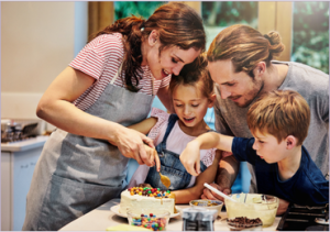 Family of four cooking decorating a cake.